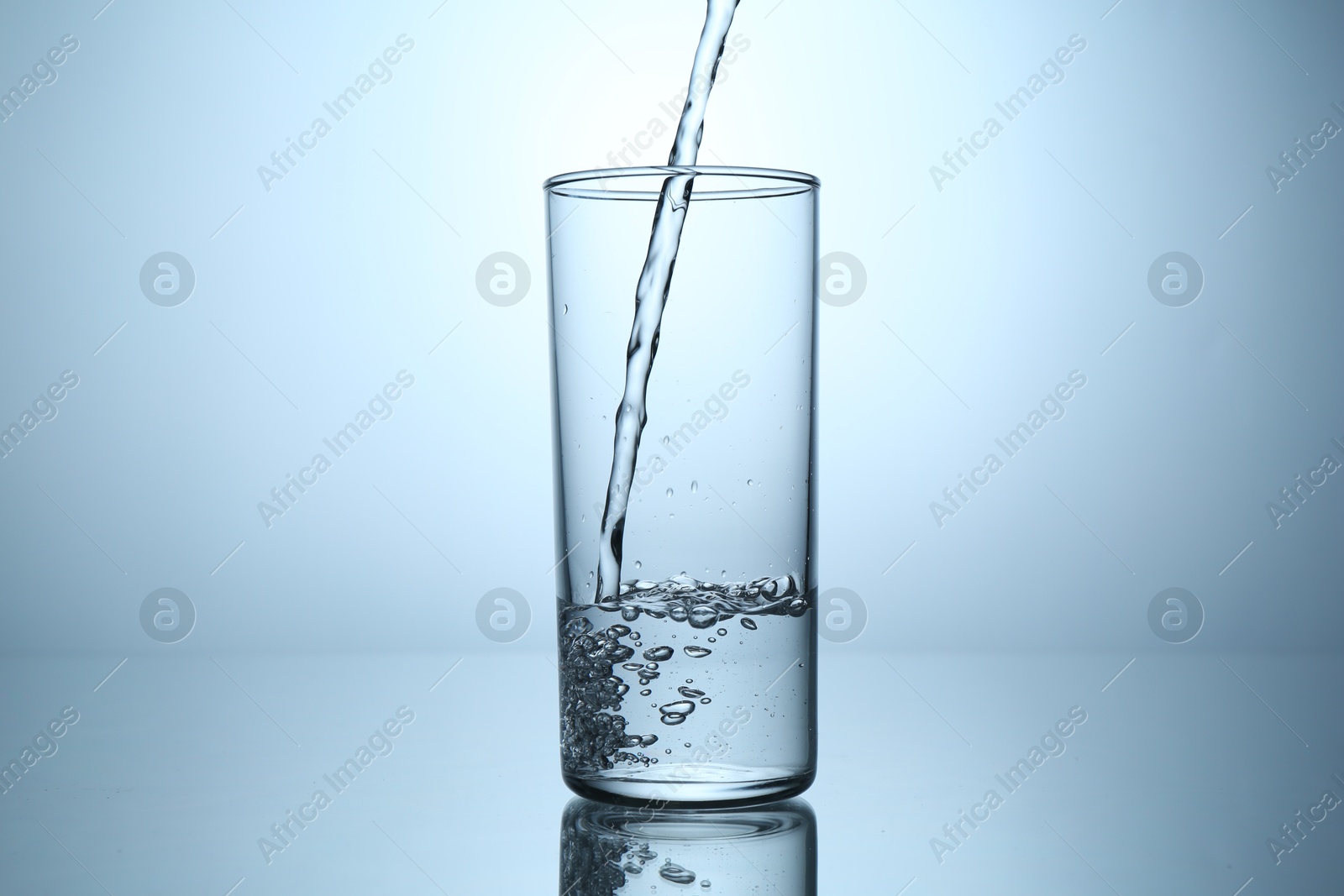 Pouring water into glass at mirror table against light grey gradient background, closeup Photo of Pouring water into glass at mirror table against light grey gradient background, closeup