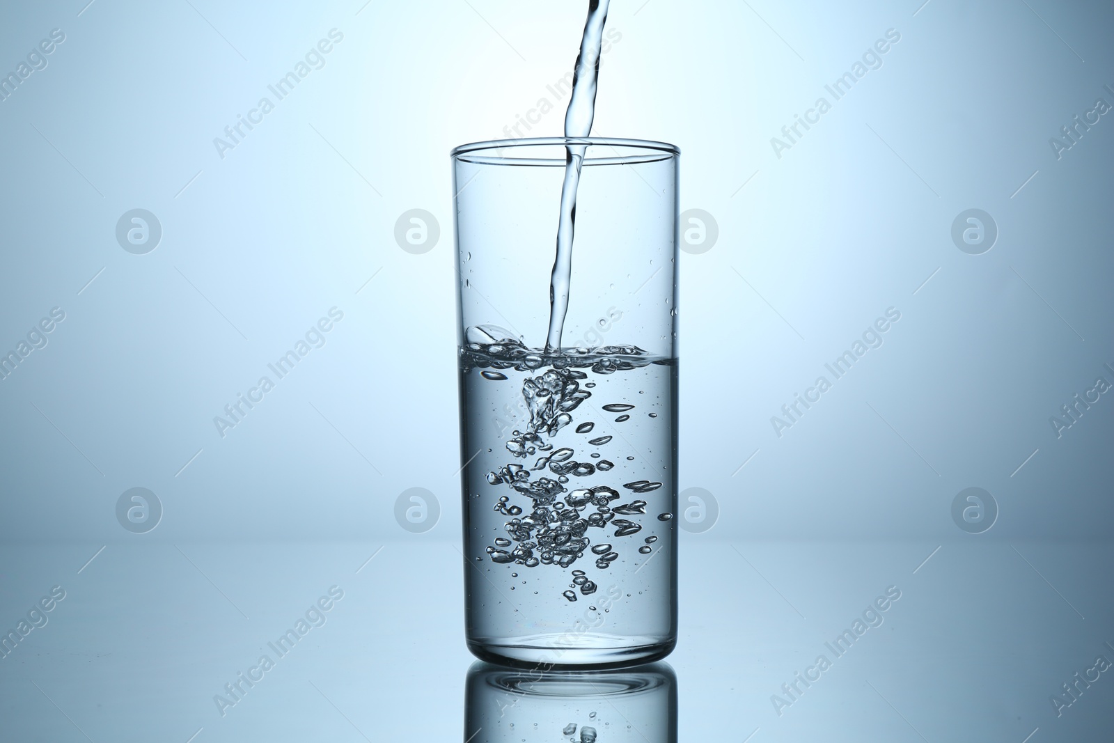 Pouring water into glass at mirror table against light grey gradient background, closeup Photo of Pouring water into glass at mirror table against light grey gradient background, closeup