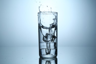 Photo of Fresh water splashing out of glass on mirror table against light grey gradient background, closeup