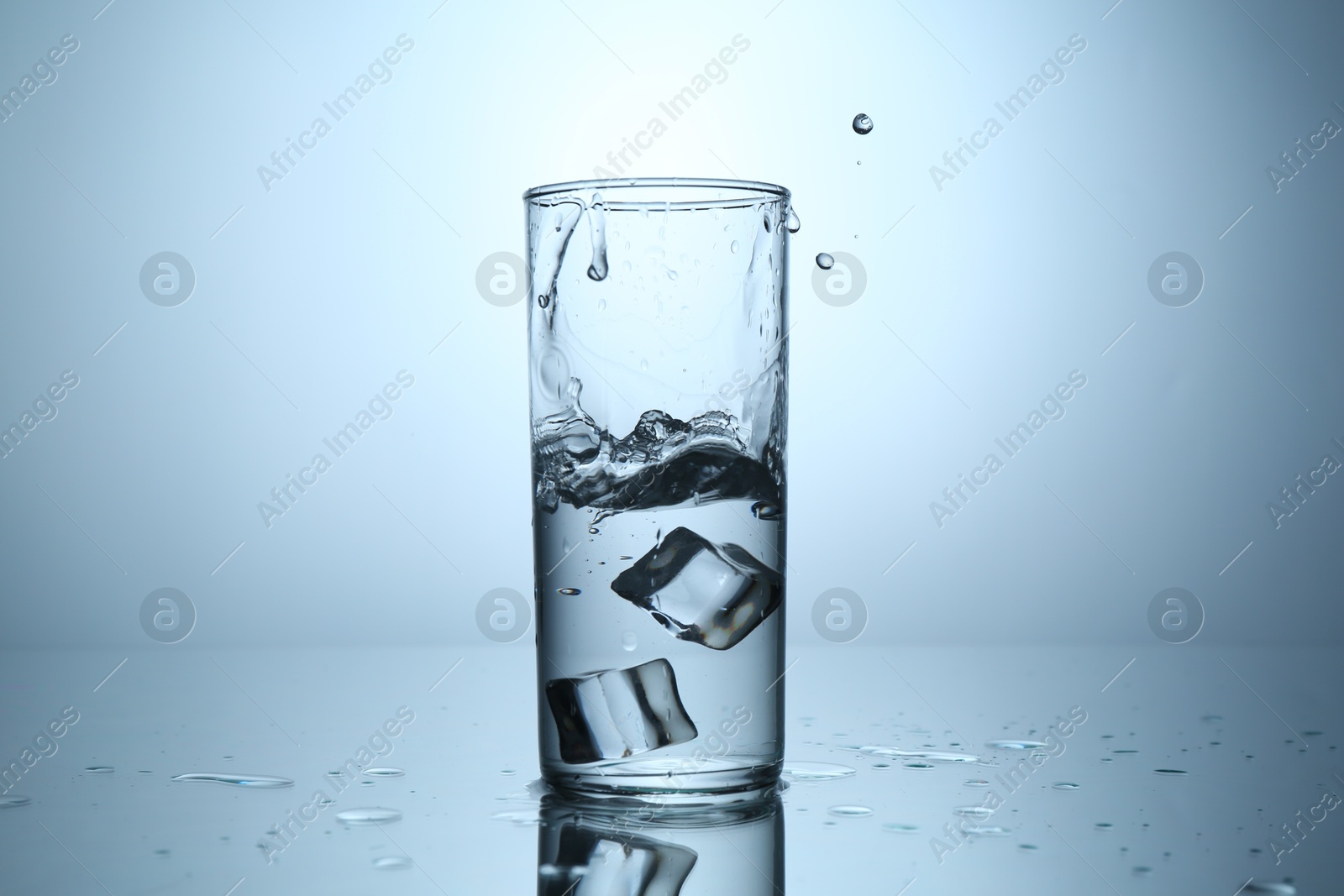 Fresh water splashing out of glass on mirror table against light grey gradient background, closeup Photo of Fresh water splashing out of glass on mirror table against light grey gradient background, closeup