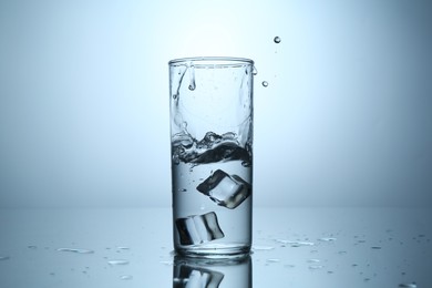 Photo of Fresh water splashing out of glass on mirror table against light grey gradient background, closeup