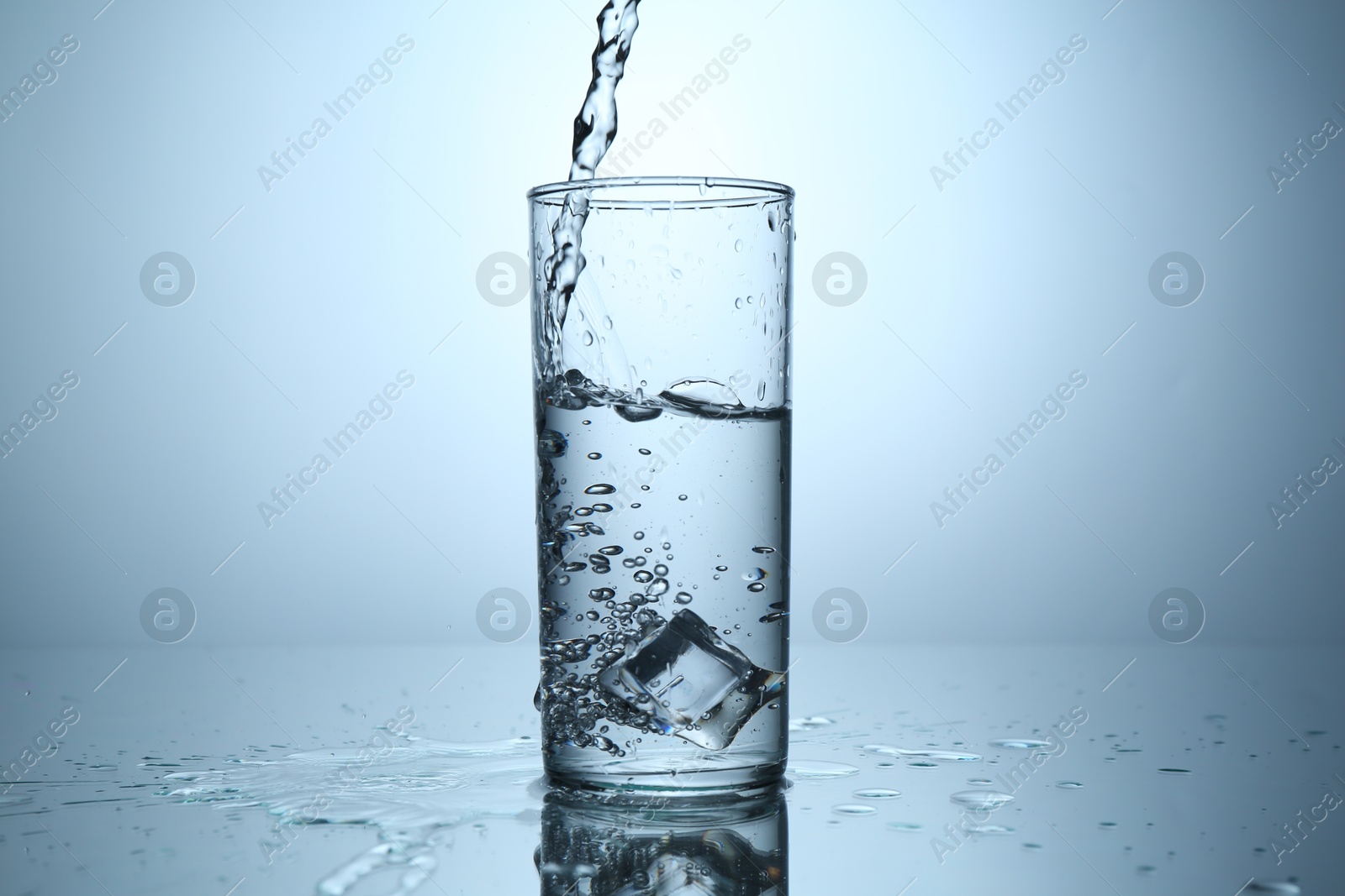 Pouring water into glass at mirror table against light grey gradient background, closeup Photo of Pouring water into glass at mirror table against light grey gradient background, closeup