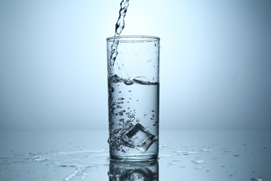 Photo of Pouring water into glass at mirror table against light grey gradient background, closeup
