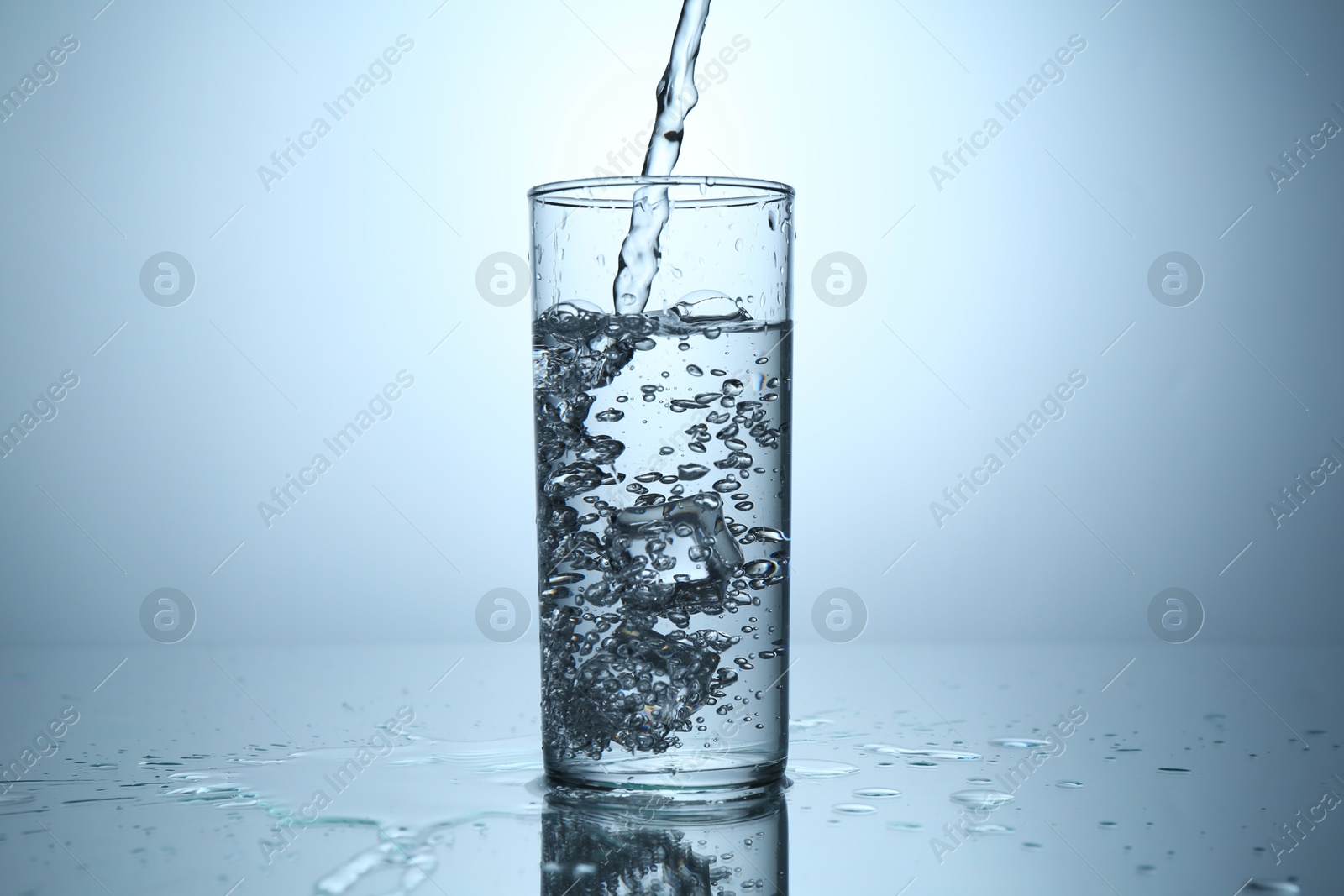 Pouring water into glass at mirror table against light grey gradient background, closeup Photo of Pouring water into glass at mirror table against light grey gradient background, closeup
