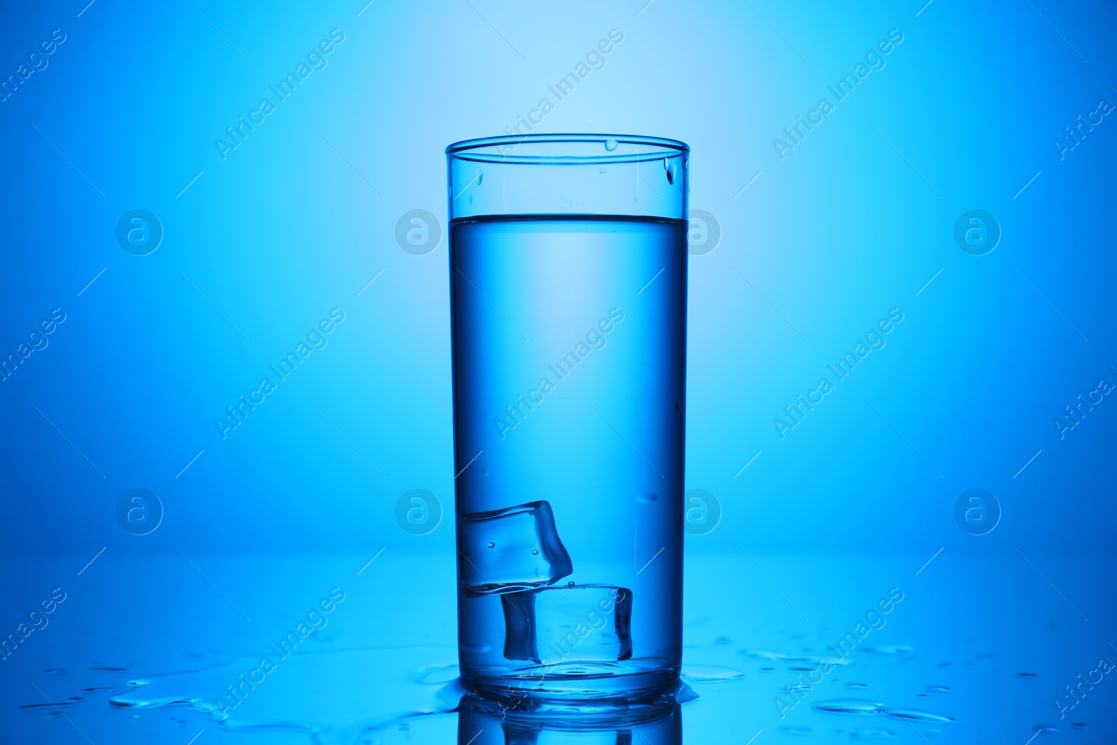Fresh water with ice cubes in glass on mirror table against blue gradient background, closeup Photo of Fresh water with ice cubes in glass on mirror table against blue gradient background, closeup