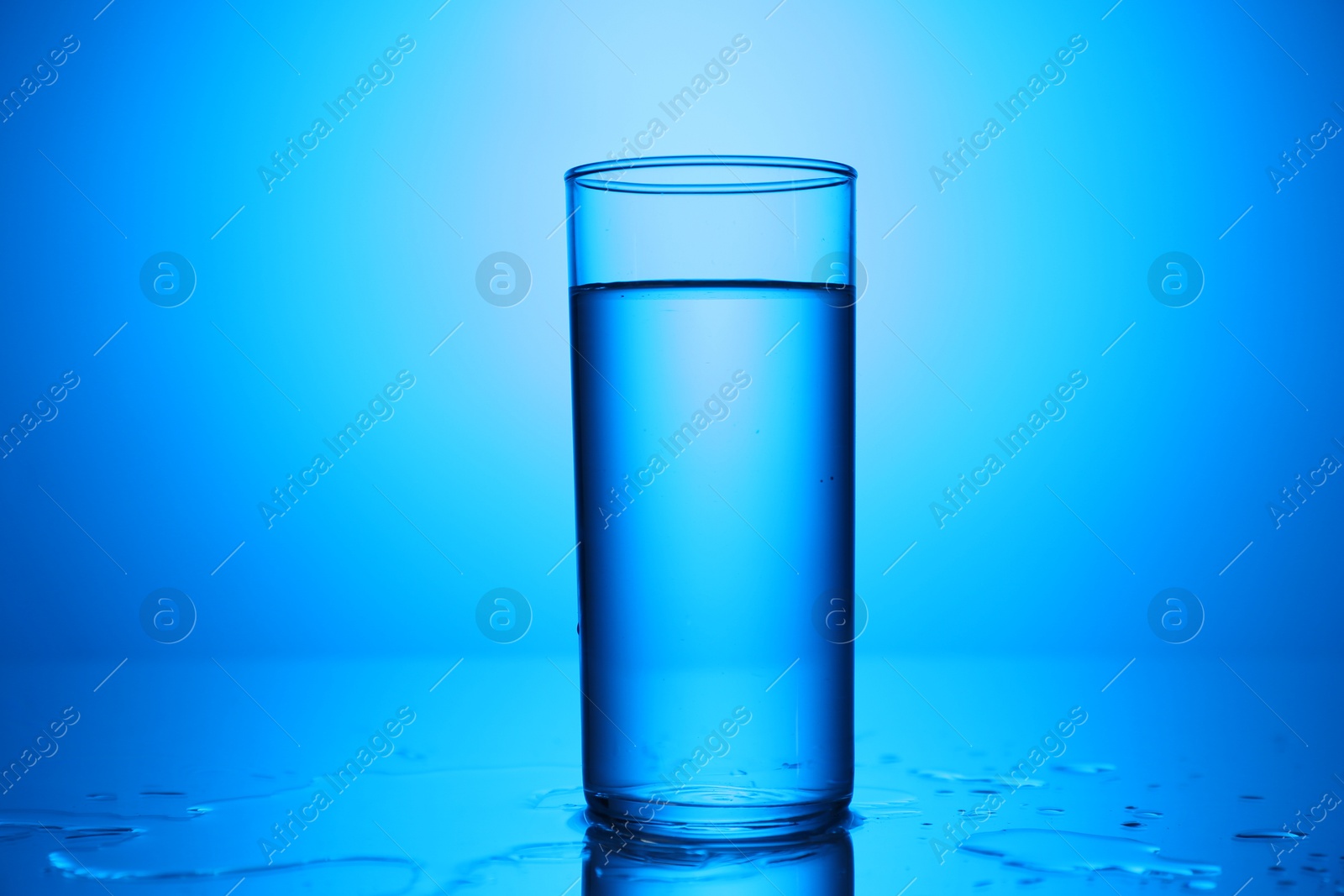 Fresh water in glass on mirror table against blue gradient background, closeup Photo of Fresh water in glass on mirror table against blue gradient background, closeup
