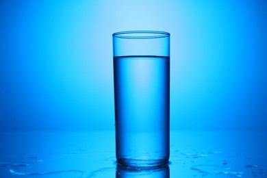 Photo of Fresh water in glass on mirror table against blue gradient background, closeup
