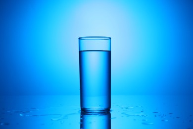 Photo of Fresh water in glass on mirror table against blue gradient background