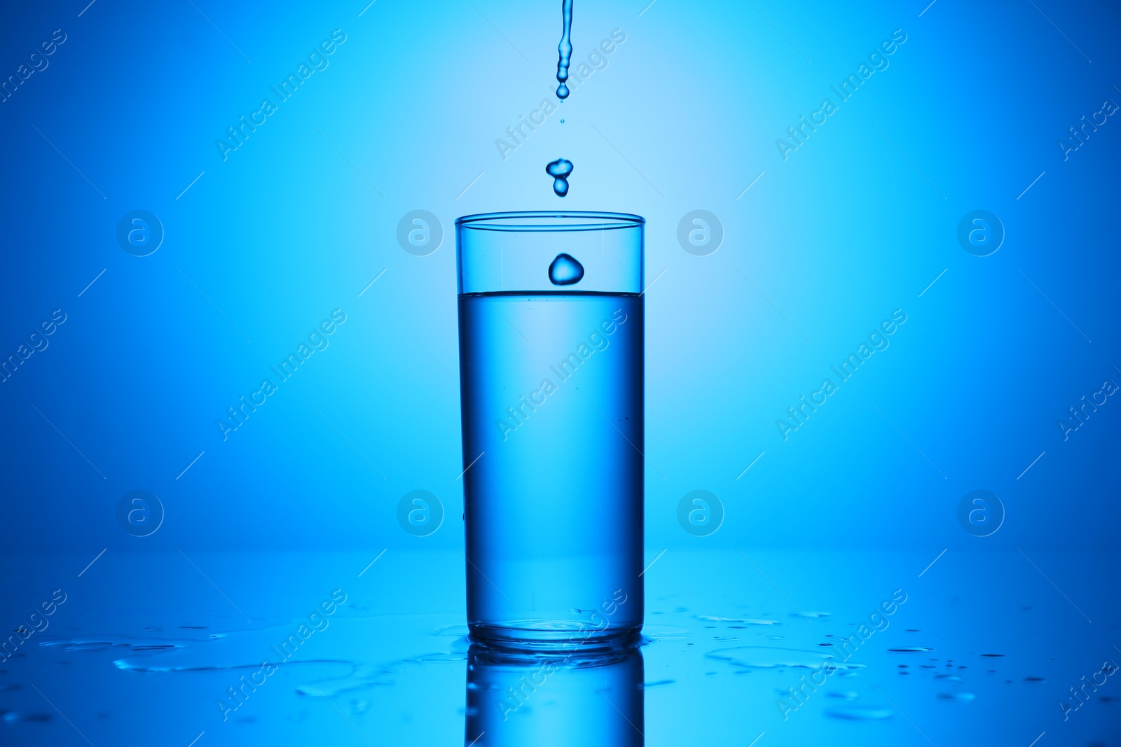 Photo of Pouring water into glass at mirror table against blue gradient background