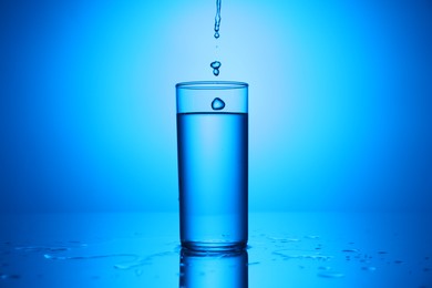 Photo of Pouring water into glass at mirror table against blue gradient background