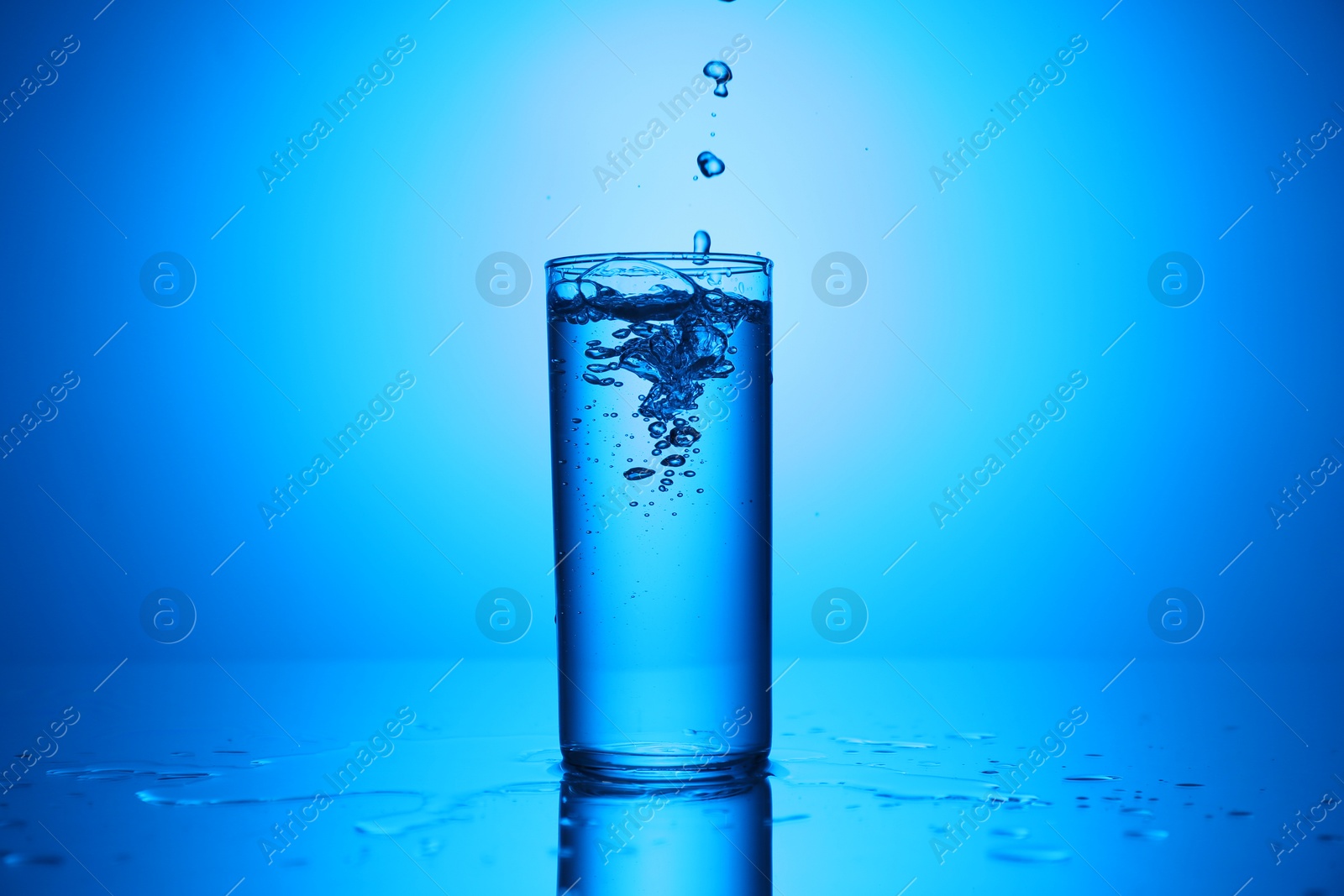 Photo of Pouring water into glass at mirror table against blue gradient background