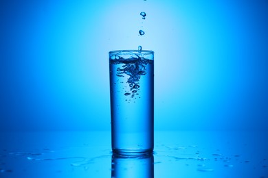 Photo of Pouring water into glass at mirror table against blue gradient background