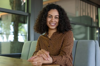 Photo of Portrait of smiling Latin American woman at table in cafe