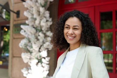 Photo of Portrait of smiling Latin American woman near building outdoors. Space for text