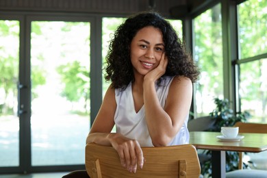 Photo of Portrait of smiling Latin American woman sitting on chair in cafe. Space for text
