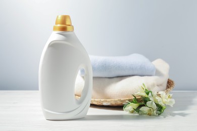 Photo of Bottle of fabric softener, clean clothes and lily flowers on white wooden table