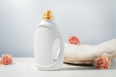 Photo of Bottle of fabric softener, clean clothes and carnation flowers on white wooden table