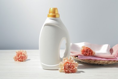 Photo of Bottle of fabric softener, clean clothes and carnation flowers on white wooden table