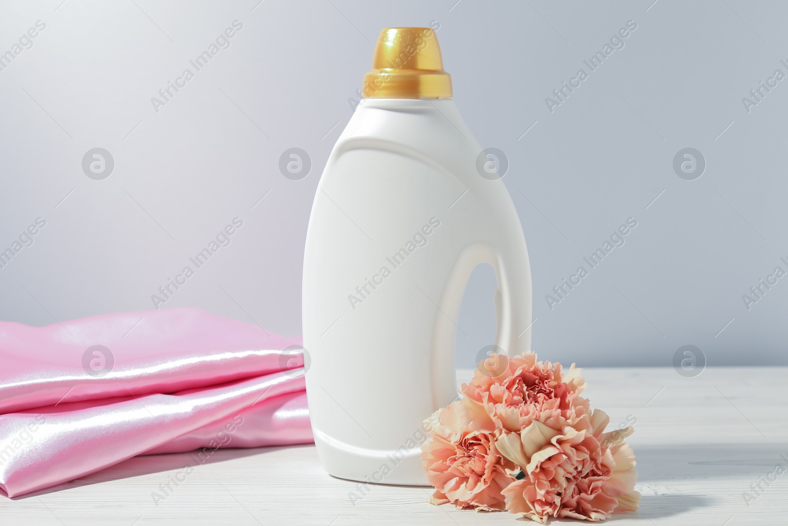 Bottle of fabric softener, clean clothes and carnation flowers on white wooden table Photo of Bottle of fabric softener, clean clothes and carnation flowers on white wooden table
