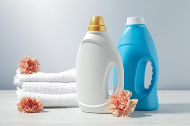 Photo of Bottles of fabric softener, terry towels and carnation flowers on white wooden table