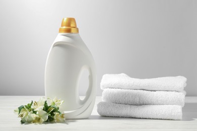 Photo of Bottle of fabric softener, terry towels and lily flowers on white wooden table