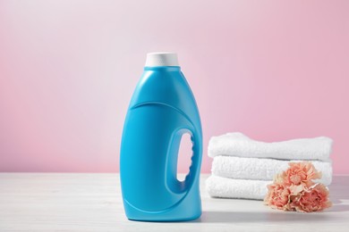Photo of Bottle of fabric softener, terry towels and carnation flowers on white wooden table against pink background