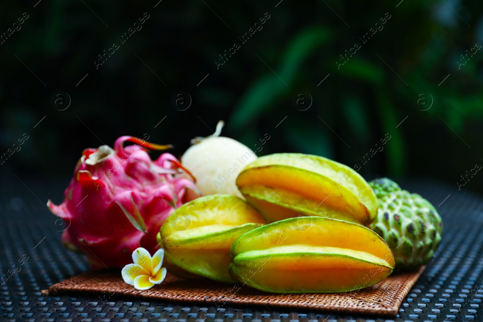 Photo of Different tropical fruit on wicker table outdoors, closeup. Space for text