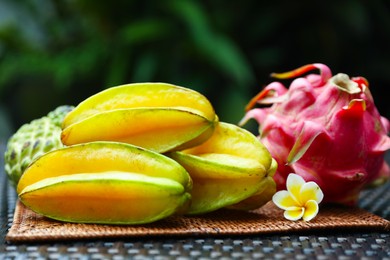Photo of Different tropical fruit on wicker table outdoors, closeup
