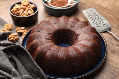 Photo of Tasty chocolate bundt cake, walnuts and cocoa powder on wooden table, closeup
