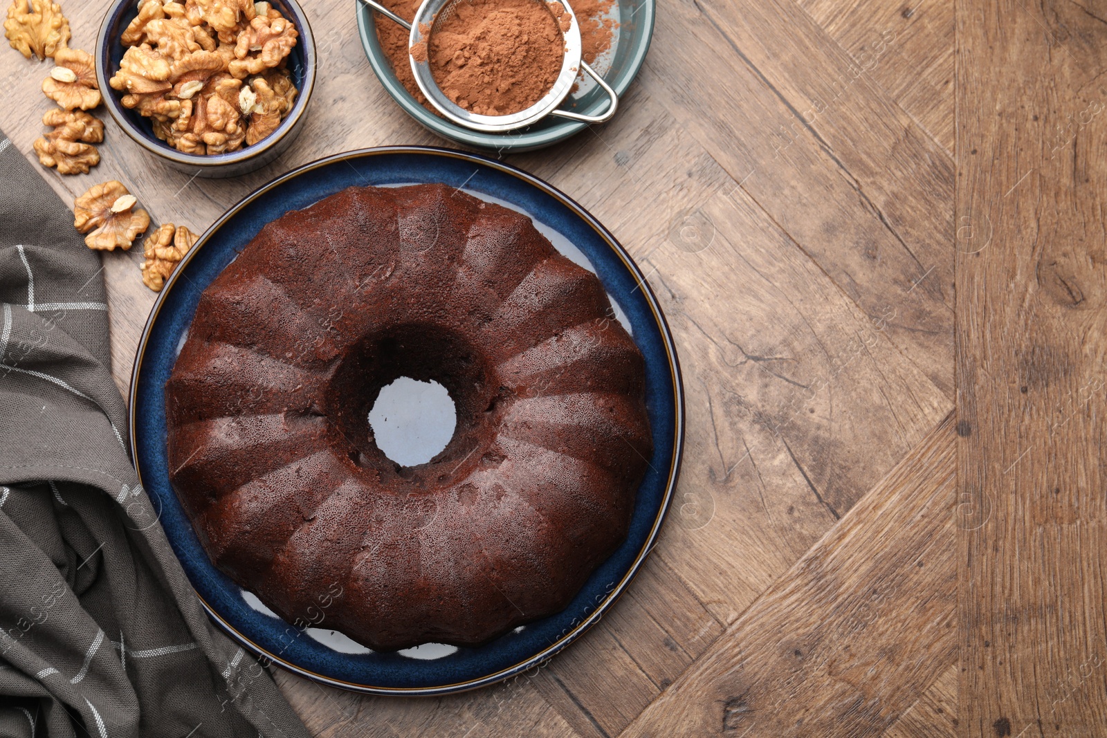 Tasty chocolate bundt cake, walnuts and cocoa powder on wooden table, flat lay. Space for text Photo of Tasty chocolate bundt cake, walnuts and cocoa powder on wooden table, flat lay. Space for text