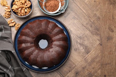 Photo of Tasty chocolate bundt cake, walnuts and cocoa powder on wooden table, flat lay. Space for text