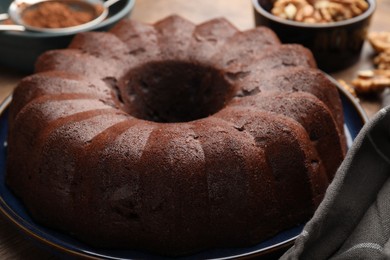Photo of Tasty chocolate bundt cake, walnuts and cocoa powder on table, closeup