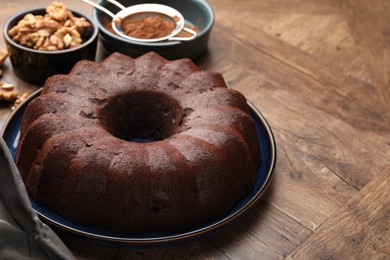 Photo of Tasty chocolate bundt cake, walnuts and cocoa powder on wooden table, closeup. Space for text