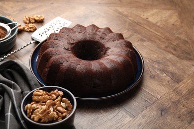 Photo of Tasty chocolate bundt cake, walnuts and cocoa powder on wooden table, closeup. Space for text