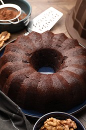 Photo of Tasty chocolate bundt cake, walnuts and cocoa powder on table, closeup