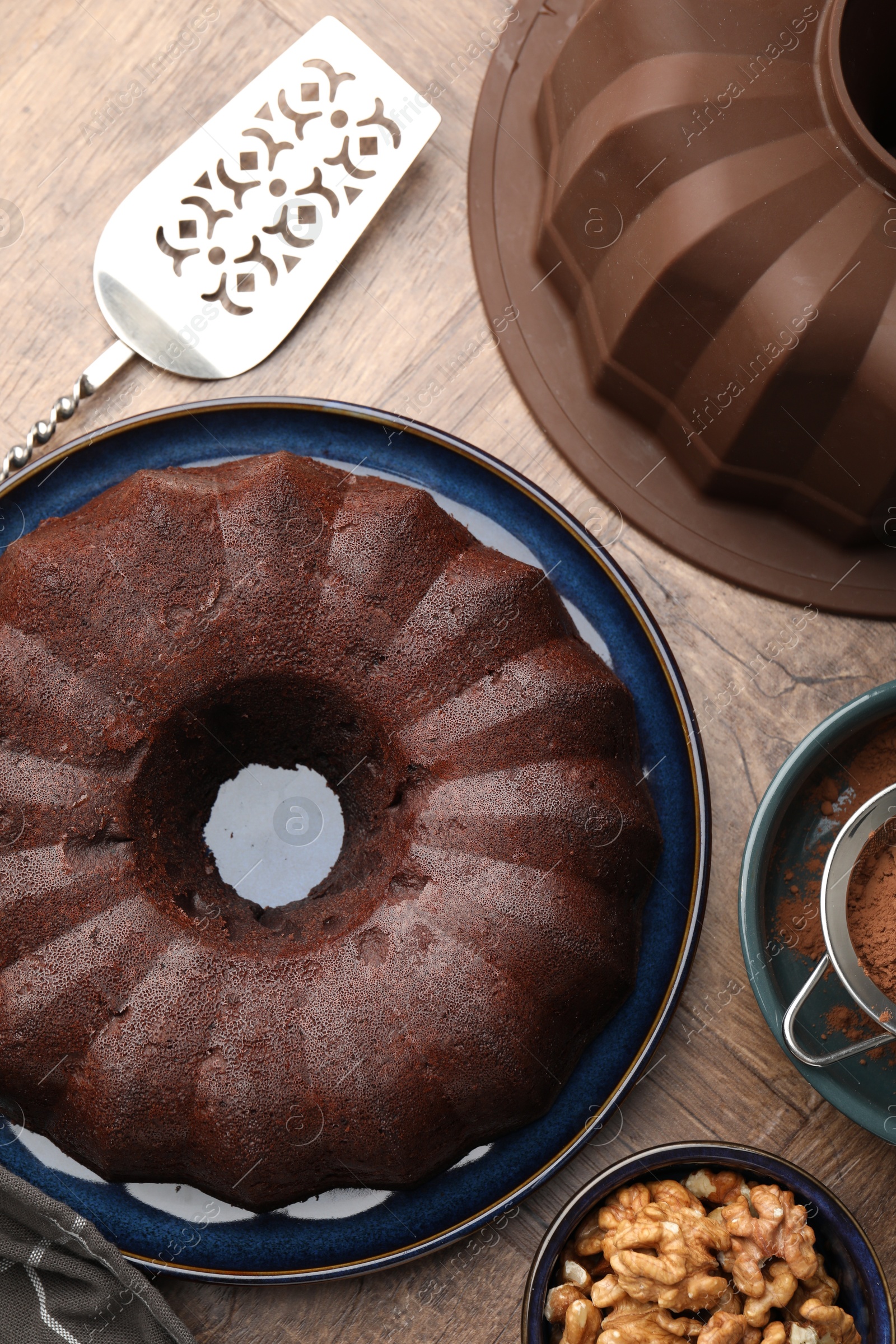 Tasty chocolate bundt cake, walnuts, cocoa powder and server on wooden table, flat lay Photo of Tasty chocolate bundt cake, walnuts, cocoa powder and server on wooden table, flat lay