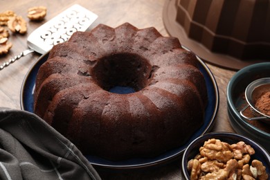 Photo of Tasty chocolate bundt cake, walnuts and cocoa powder on table, closeup