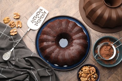 Photo of Tasty chocolate bundt cake, walnuts and cocoa powder on wooden table, flat lay