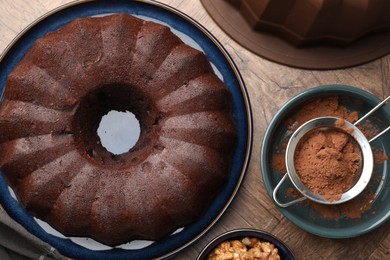 Photo of Tasty chocolate bundt cake, walnuts and cocoa powder on wooden table, flat lay