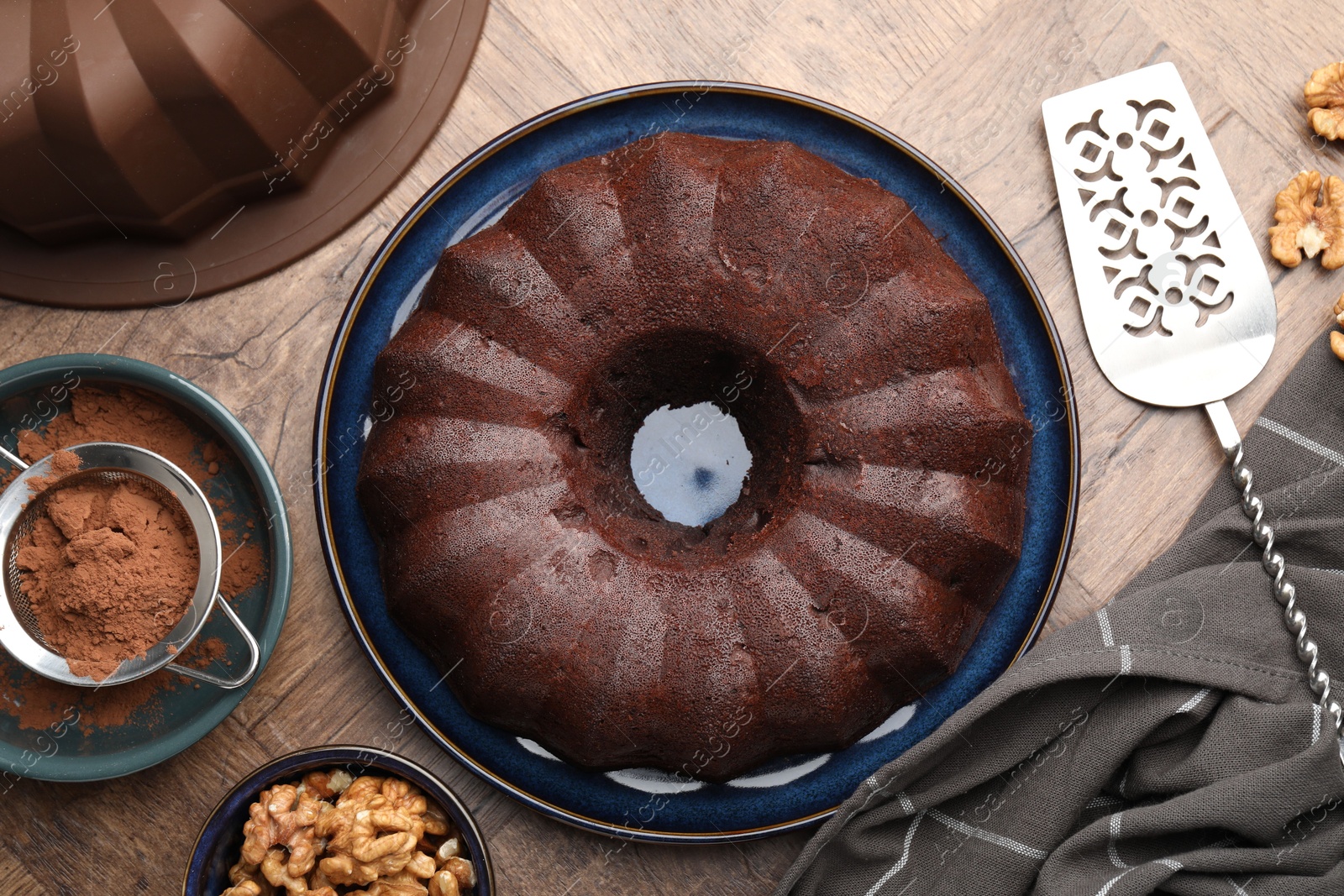 Tasty chocolate bundt cake, walnuts and cocoa powder on wooden table, flat lay Photo of Tasty chocolate bundt cake, walnuts and cocoa powder on wooden table, flat lay