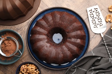 Photo of Tasty chocolate bundt cake, walnuts and cocoa powder on wooden table, flat lay