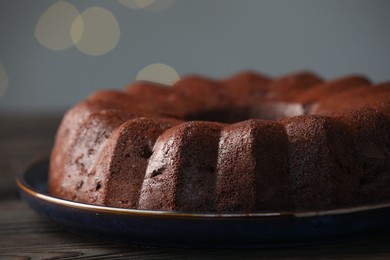 Photo of Tasty chocolate bundt cake on wooden table, closeup. Bokeh effect
