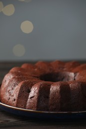 Photo of Tasty chocolate bundt cake on wooden table, closeup. Bokeh effect