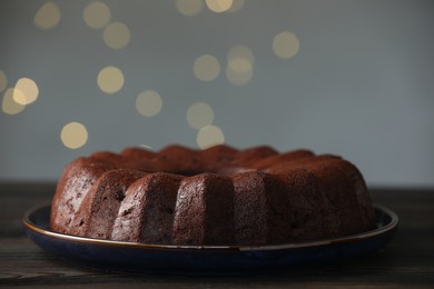Photo of Tasty chocolate bundt cake on wooden table, closeup. Bokeh effect