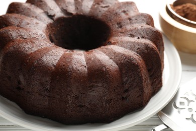 Photo of Tasty chocolate bundt cake, cocoa powder and server on table, closeup
