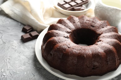Photo of Tasty bundt cake and pieces of chocolate on grey table, closeup. Space for text