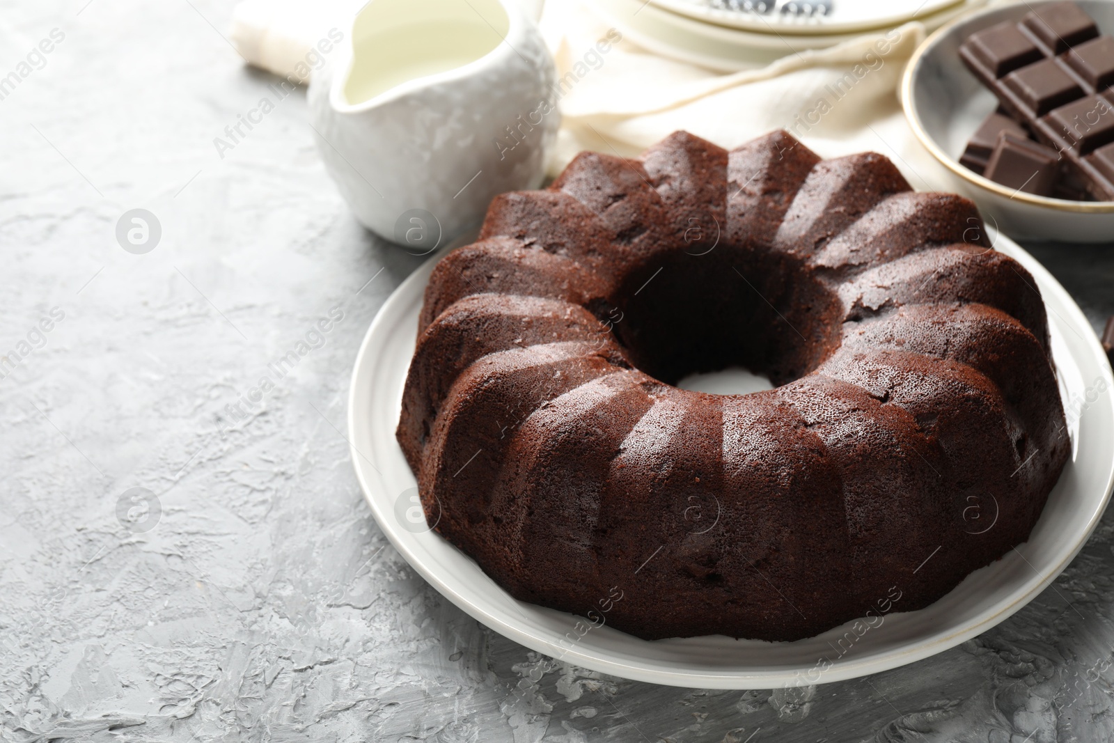 Tasty bundt cake, pieces of chocolate and milk on grey table, closeup. Space for text Photo of Tasty bundt cake, pieces of chocolate and milk on grey table, closeup. Space for text