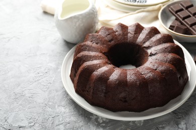Photo of Tasty bundt cake, pieces of chocolate and milk on grey table, closeup. Space for text