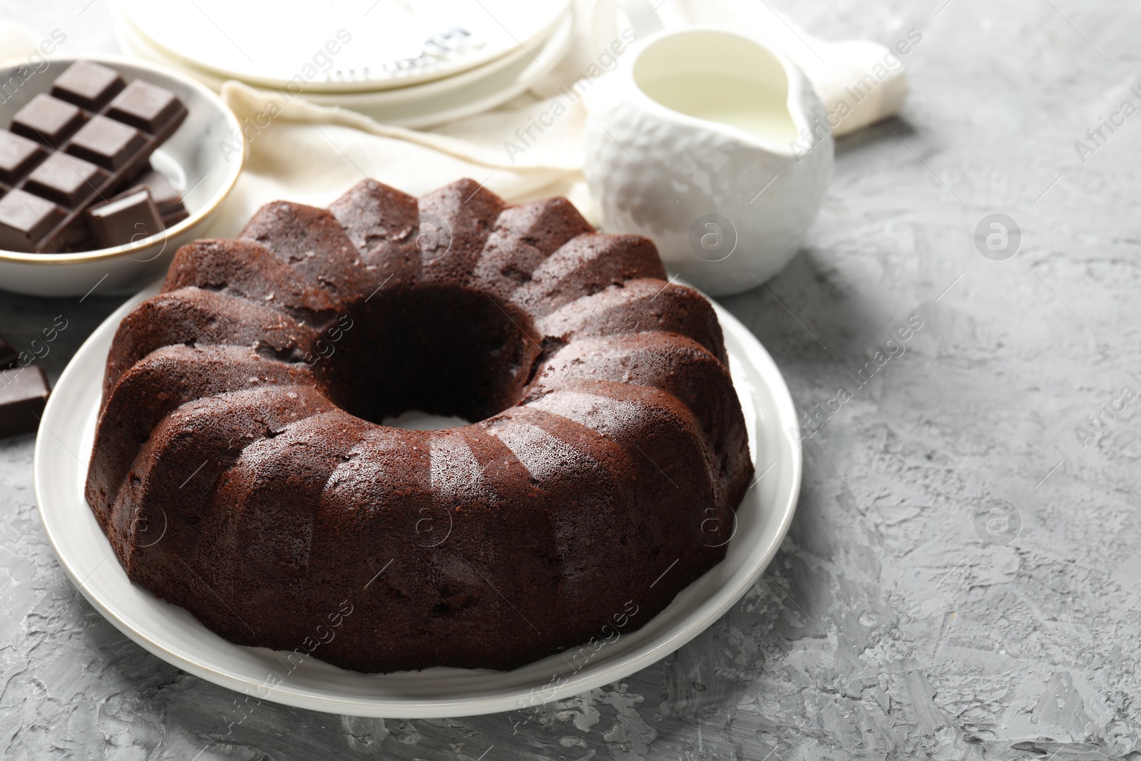 Tasty bundt cake, pieces of chocolate and milk on grey table, closeup. Space for text Photo of Tasty bundt cake, pieces of chocolate and milk on grey table, closeup. Space for text