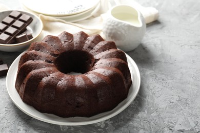 Photo of Tasty bundt cake, pieces of chocolate and milk on grey table, closeup. Space for text